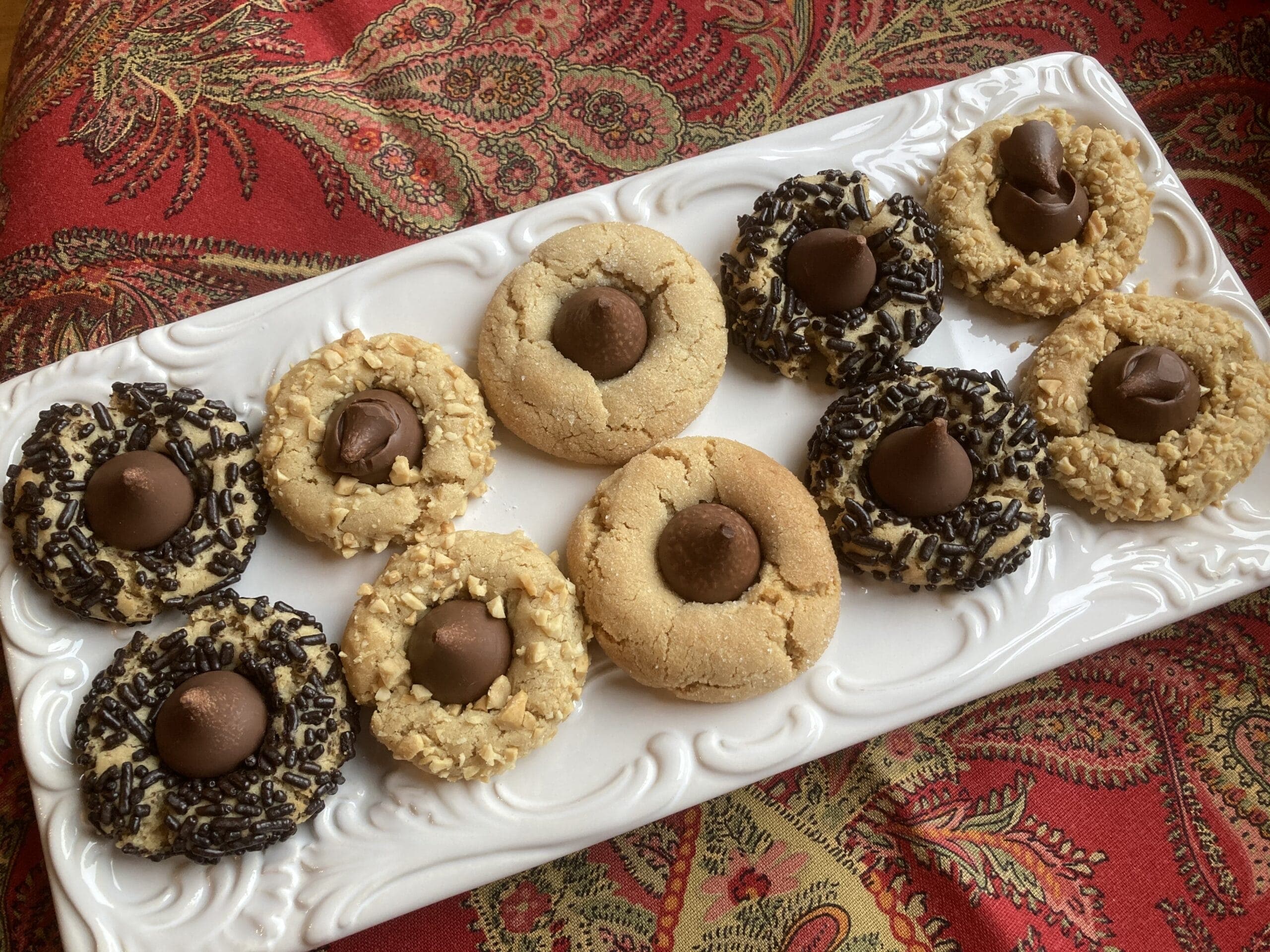 A white platter holds an assortment of cookies topped with chocolate, including some with sprinkles and others plain.