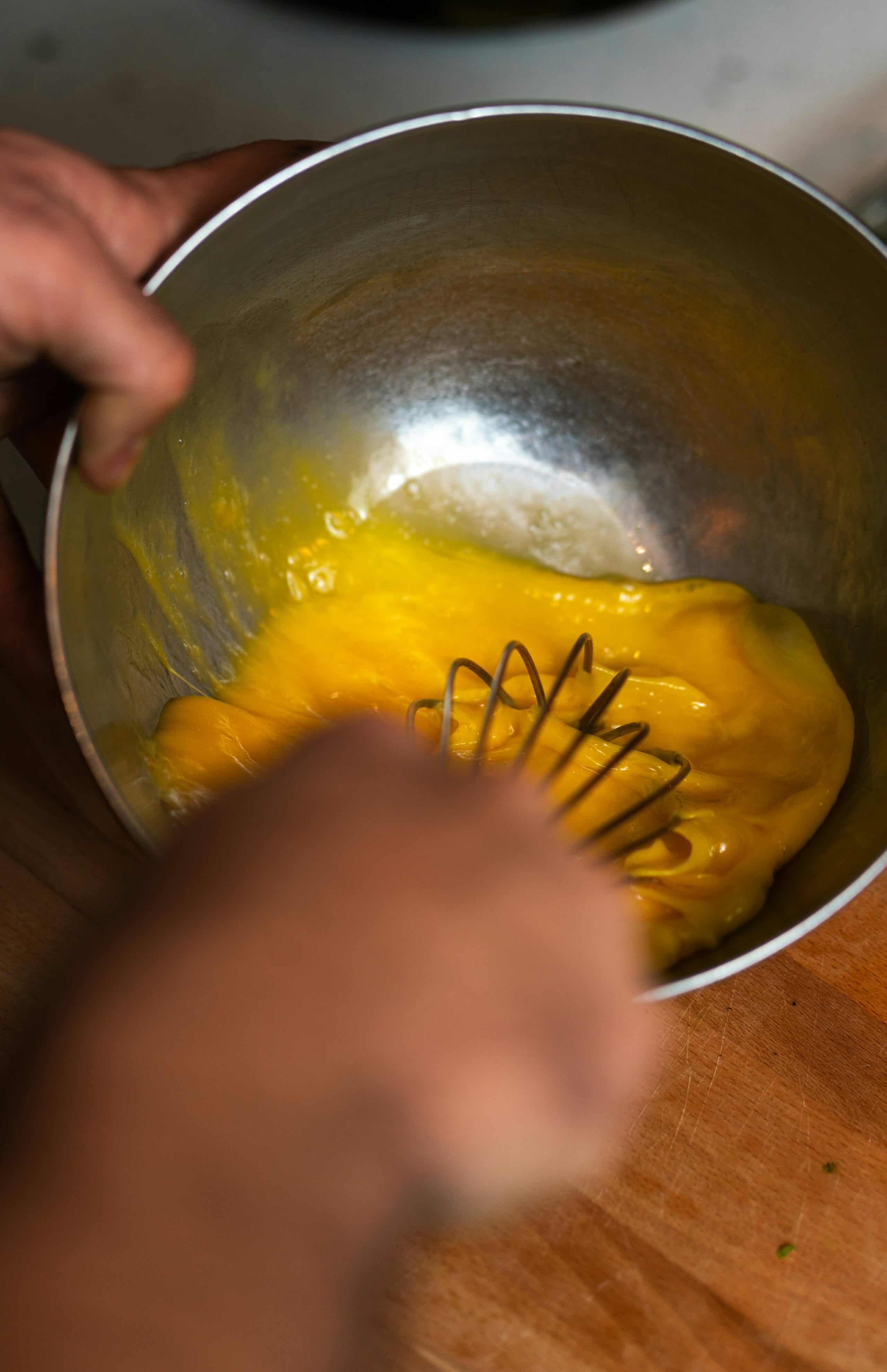 A hand whisking eggs in a metal bowl.