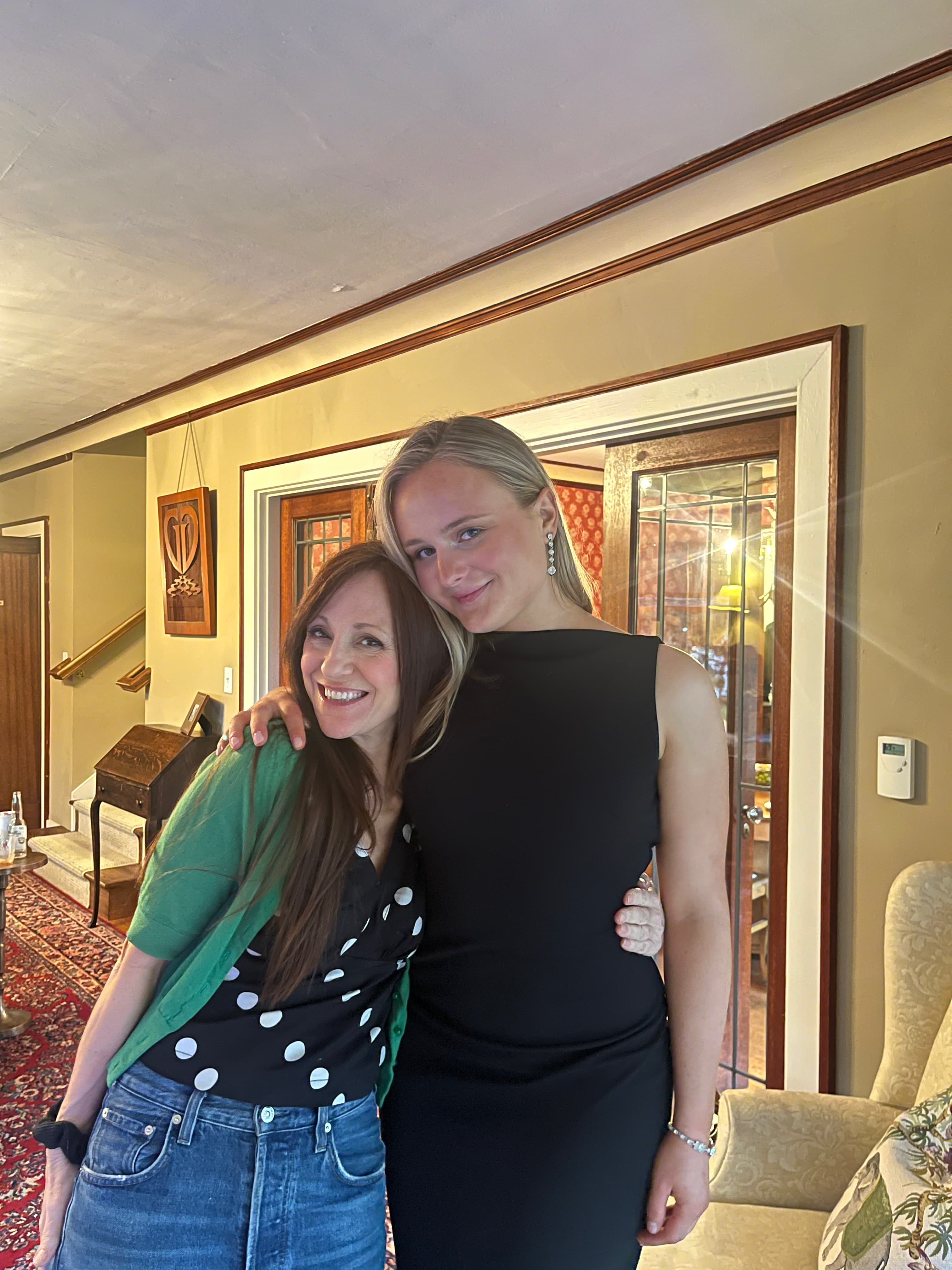 Two women smiling together in a warmly lit room with decorative elements in the background.