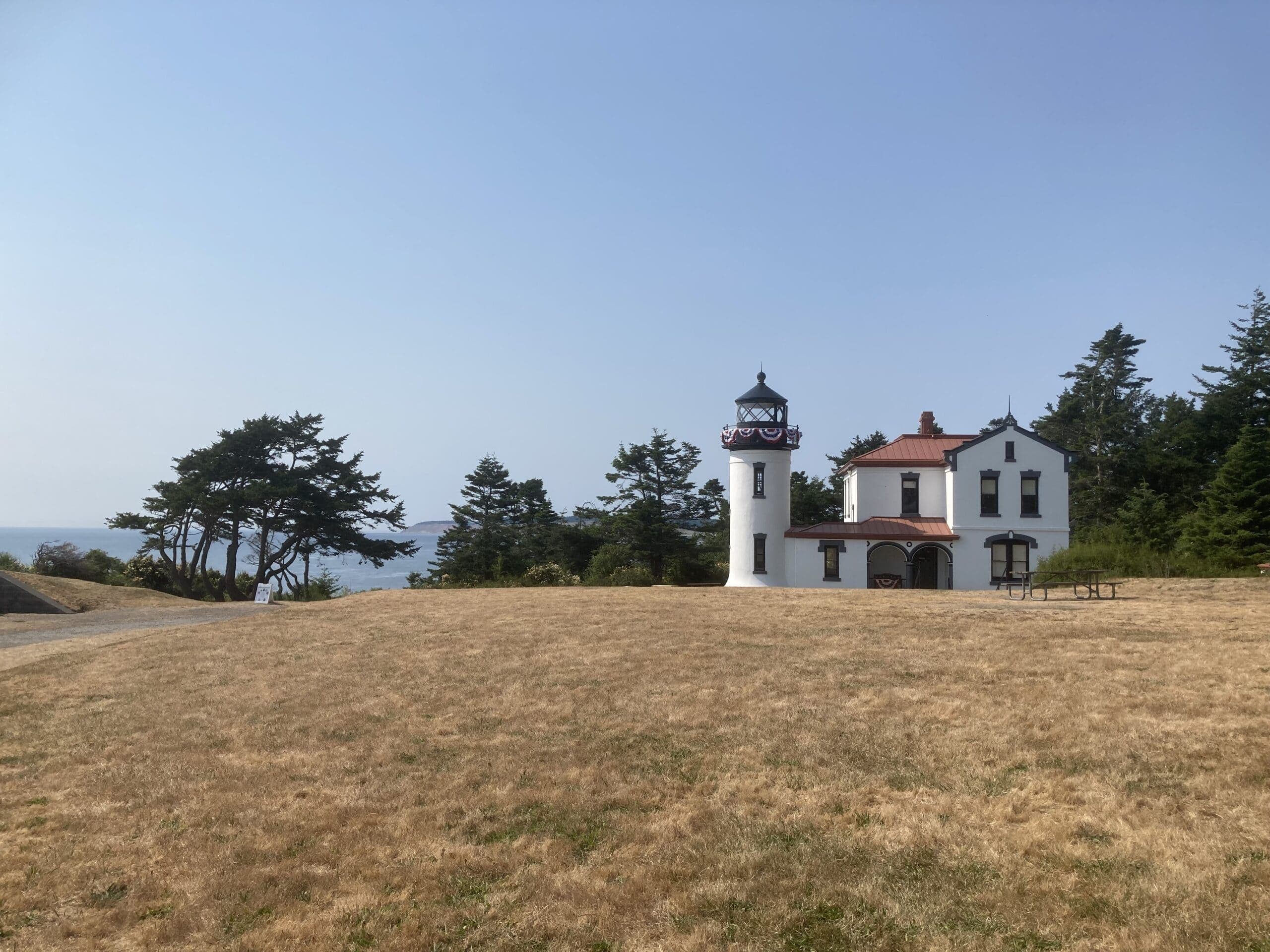 A white lighthouse beside a historic house on a grassy hillside overlooking the ocean. A white lighthouse beside a historic house on a grassy hillside overlooking the ocean.