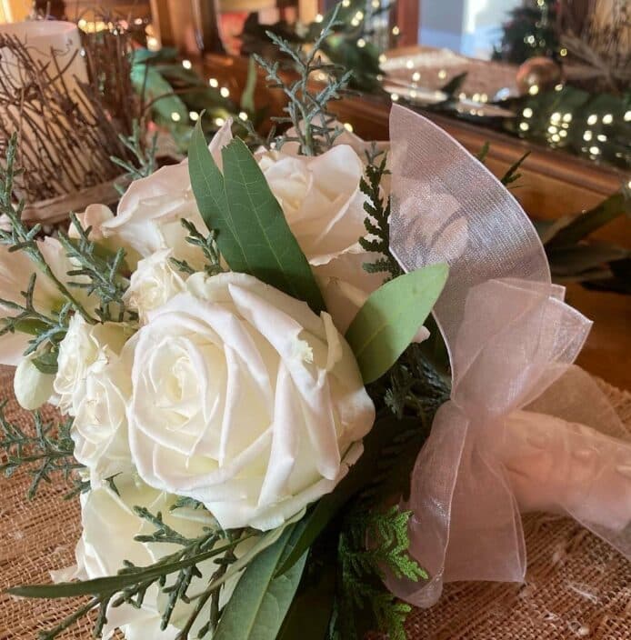 A bouquet of white roses and greenery tied with a sheer ribbon.