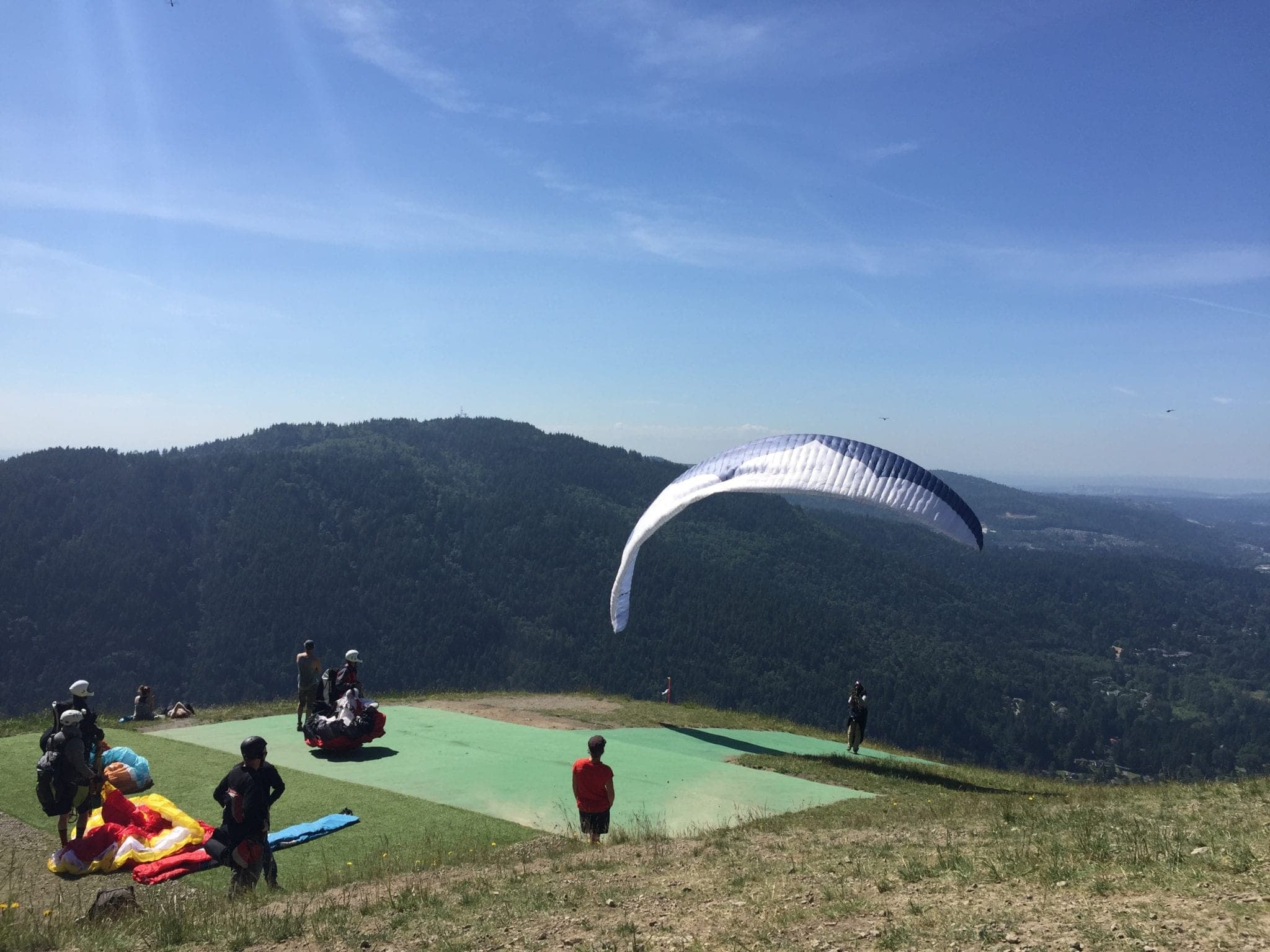 A paraglider takes off from a grassy launch site overlooking a mountainous landscape. A paraglider takes off from a grassy launch site overlooking a mountainous landscape.