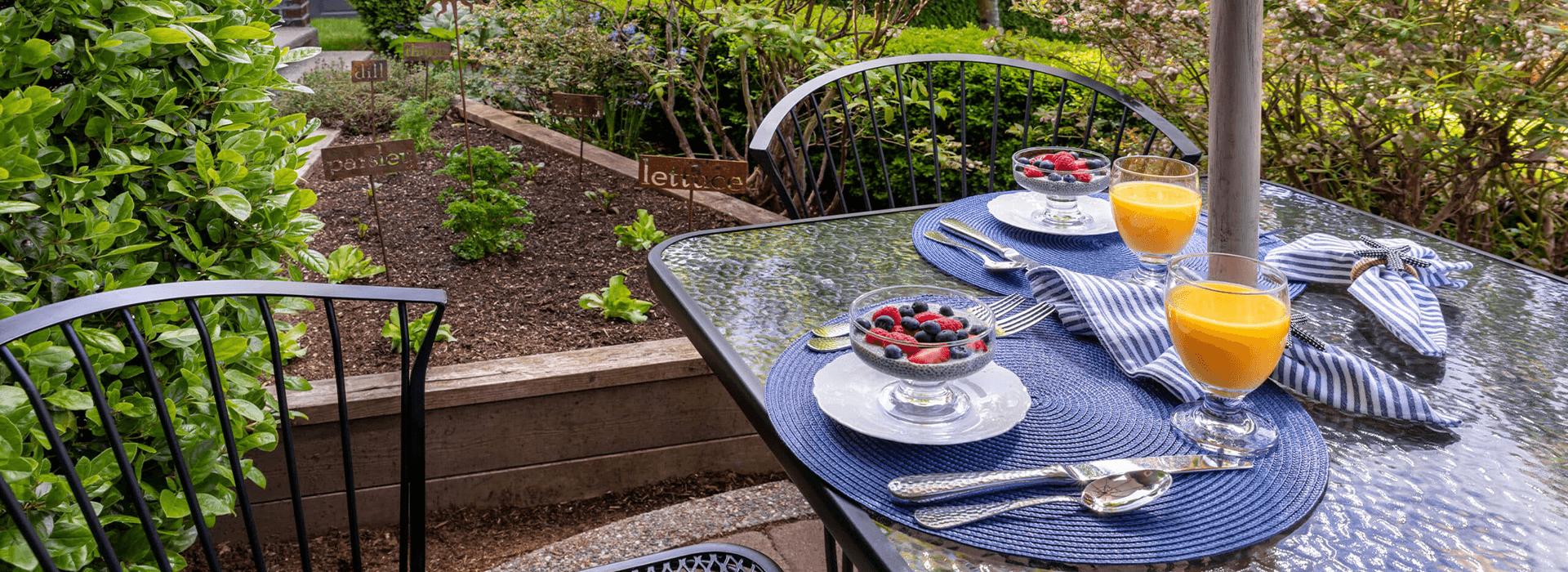 A beautifully set outdoor table with fresh fruit, orange juice, and a view of a garden.