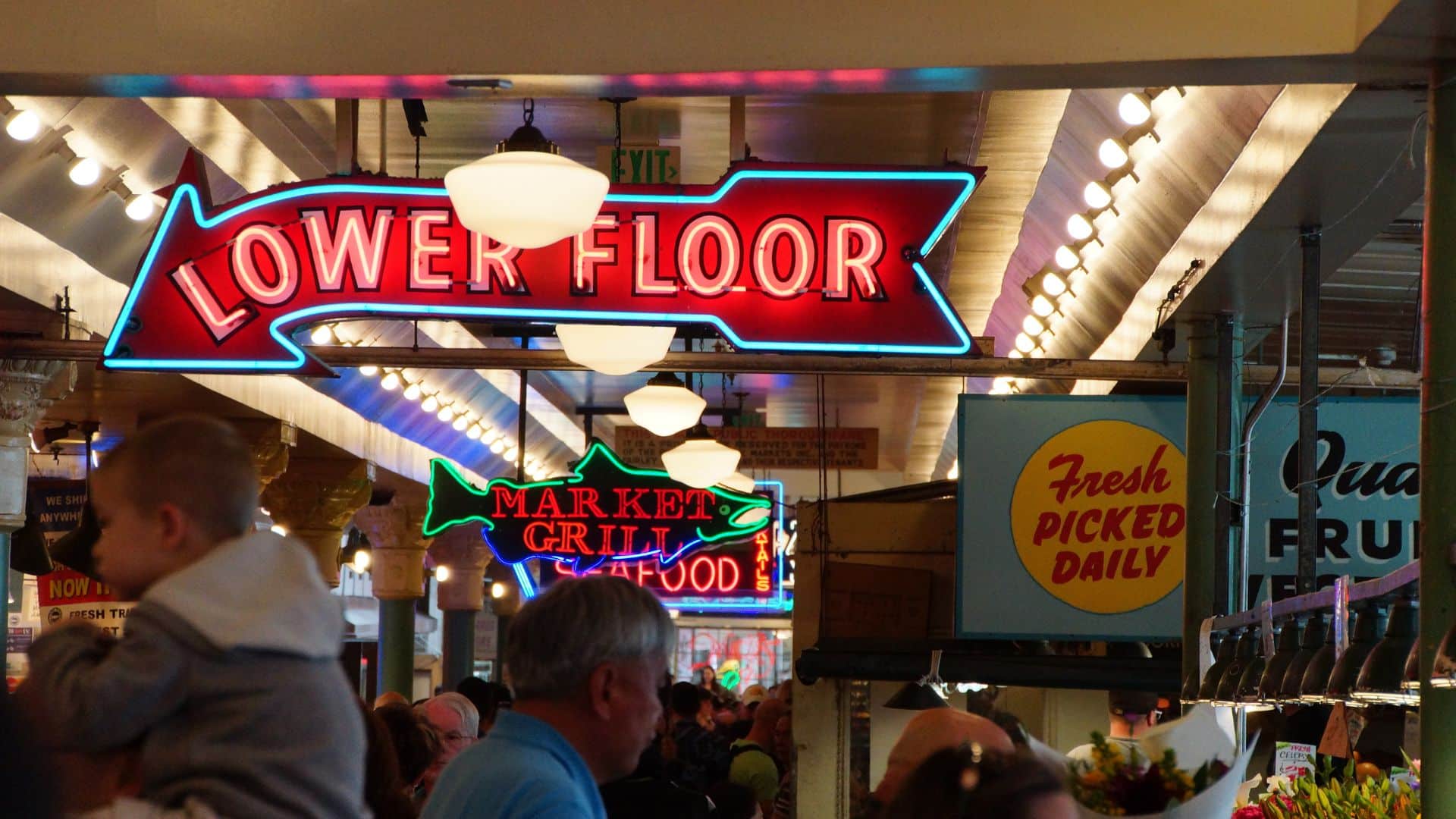 View down the main aisle in Pike Place Market, bustling with people and light-up neon signs