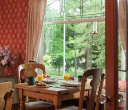 The dining area at Greenlake guesthouse is immaculate with amazing light coming into the room, flowers, red patterned wallpaper, orange juice, and a tasty breakfast meal